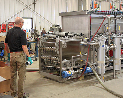 Technician loading canisters on tunnel style industrial parts washer.