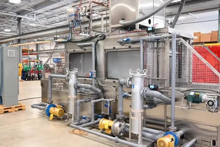 Industrial washing system with pumps, pipes, and enclosures inside a manufacturing facility.