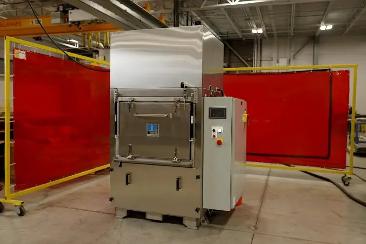 Large industrial washing machine with control panel in a factory setting, surrounded by red safety barriers.