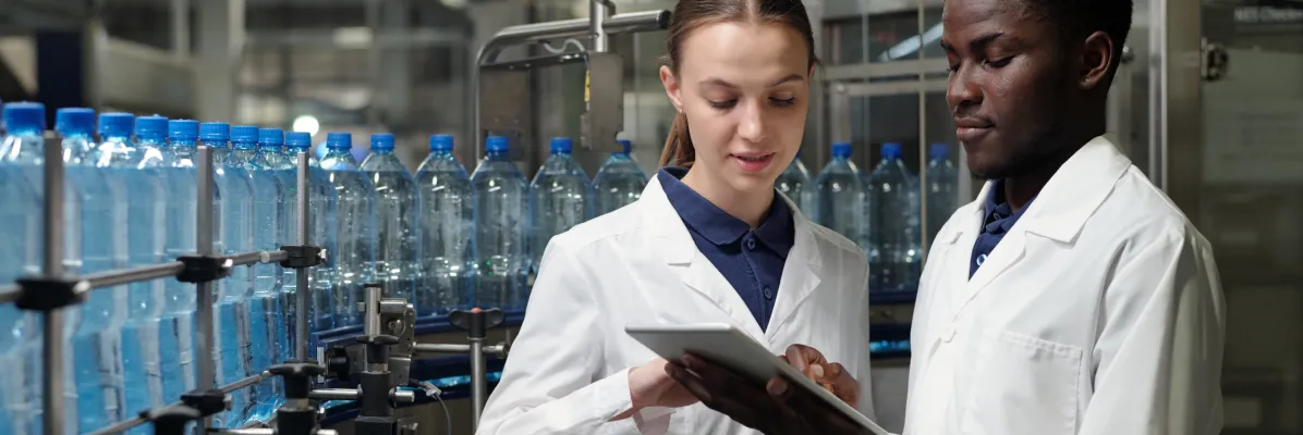 Two quality control technicians reviewing 3-A sanitary standards on a tablet at a bottling facility.