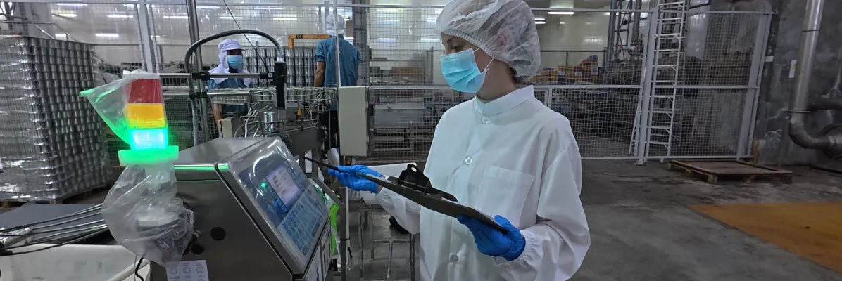 Food safety worker in PPE reviewing sanitary design principles on a clipboard at a processing facility.