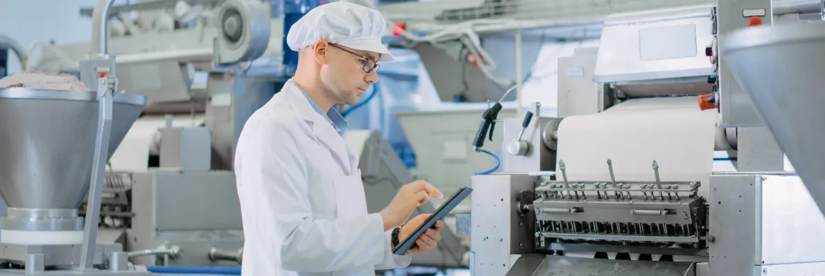 Food manufacturing inspector using a tablet to audit sanitary process equipment on a production line.